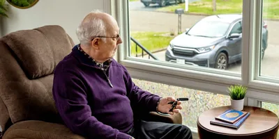 An older brother sitting by a window and looking out at his car. He holds his car keys in his hand as he meditates.