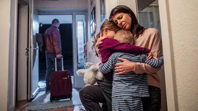 A father with a suitcase leaving his home. The mother embraces her two crying children.