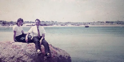 Winston and Pam Payne, in younger years, sit on top of a rock by the sea