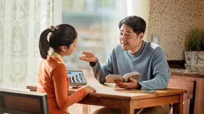 A father kindly using the Bible to reason with his daughter. Her tablet displays the theoretical stages of human evolution.