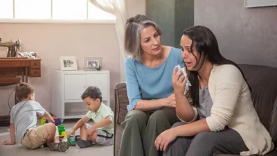 A sister listening empathetically to a single mother in distress. The mother’s two young sons play in another room.