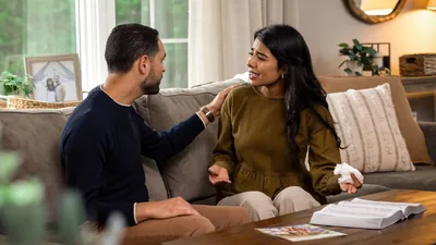 The same couple having an emotional conversation at home. The wife, in tears, expresses herself as her husband calmly listens with his hand on her shoulder. An open Bible and the brochure “Your Family Can Be Happy” lie on the table in front of them.