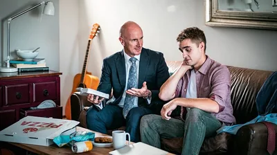 An elder, holding a Bible, giving a young brother counsel regarding cleanliness. The young brother’s apartment is unkempt.