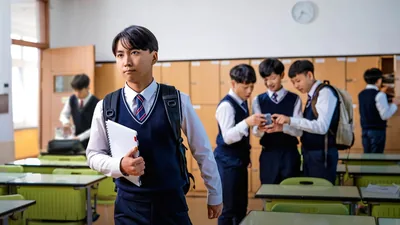 A young brother at school, confidently walking away from his classmates who are looking at something on a smartphone.