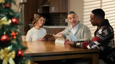 The couple from the previous image, studying the “Enjoy Life Forever!” brochure with the man at his home. The Christmas tree is nearby.