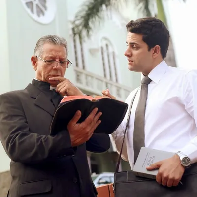 A clergyman looking carefully at a scripture in his Bible while a brother witnesses to him.