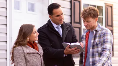 A couple in the door-to-door ministry, reading a scripture to a young man.