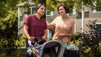 A downcast sister with her baby in a stroller, working in the ministry with another sister who has her arm around her.