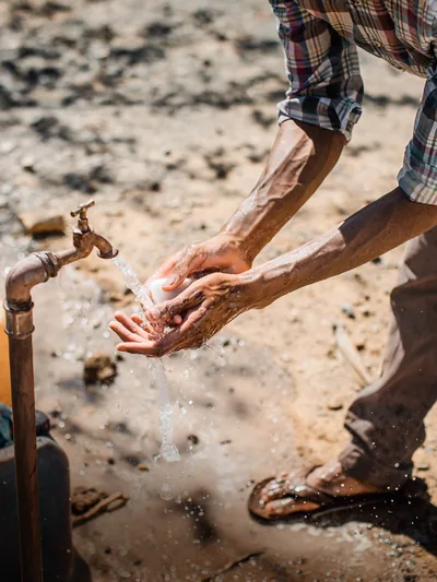 A man washing his hands with soap and water outdoors.