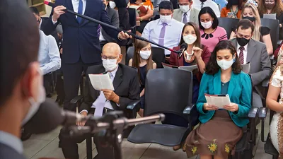 A sister commenting at a congregation meeting. A brother holds a boom microphone for her. All in attendance are wearing masks.
