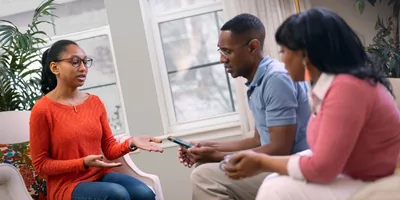 A teenage girl showing her phone to her parents and expressing her feelings to them. Her parents are listening intently.