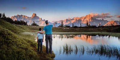 A father and son standing by a lake and looking at the mountains in the distance.