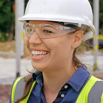 A scene from the video “Enter the Door to Activity in Faith​—Assist With a Theocratic Building Project.” Sarah wears a hard hat and a big smile at a construction site.