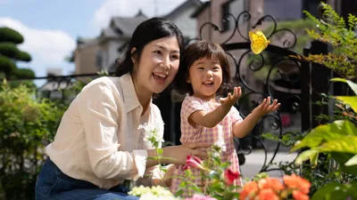 A mother and her young daughter happily watching a butterfly outside their home.