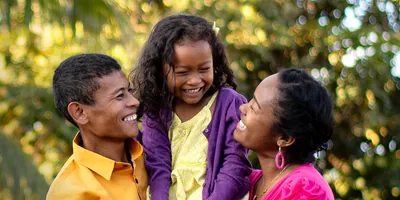 A father and mother happily embracing their young daughter.