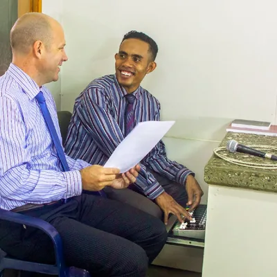Benjamin talks with a local Christian brother at a sound console in a Kingdom Hall