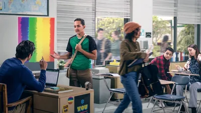 A teenage Witness respectfully explaining his beliefs to a teacher in a classroom. The classroom is decorated with rainbow flags to support gay rights.