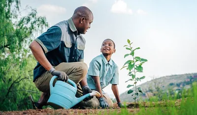 A father helps his son to water a plant