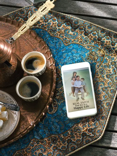 A smartphone lying next to two cups of coffee. The brochure ‘Real Faith​—Your Key to a Happy Life’ is displayed on the smartphone.