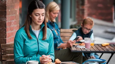 The same sister praying as she sits at a table at a café. At a nearby table is a woman with her young son.