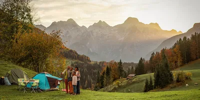 A family camping in the mountains. The family is taking a selfie with the mountains in the background.