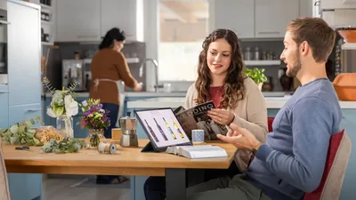 An engaged couple discussing whether they will serve alcohol at their wedding reception. They have an open Bible on the table along with a tablet that displays multiple bottles of wine.