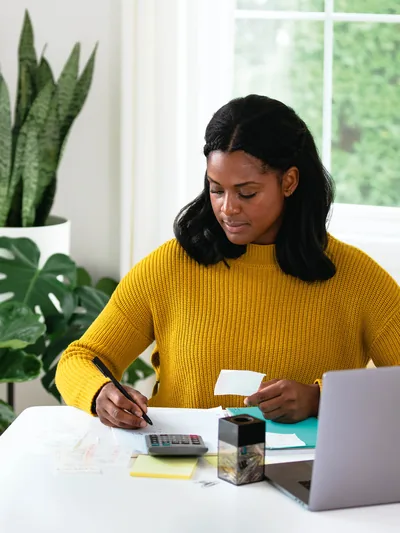 A woman using a calculator and recording details from a receipt.