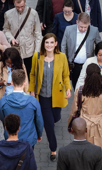 A young woman smiles and confidently walks along a crowded sidewalk