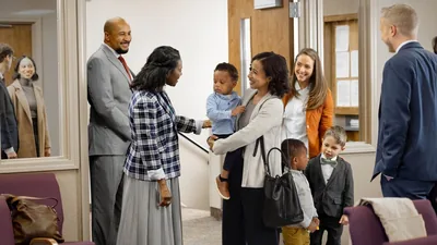 The mother from the previous image enjoying the warm welcome she is receiving from brothers and sisters at the Kingdom Hall. She holds her younger son while her older son speaks with a young boy.