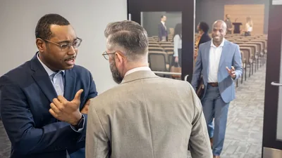 Two brothers conversing with each other at the Kingdom Hall. One of the brothers speaks negatively about another brother who is walking toward them.