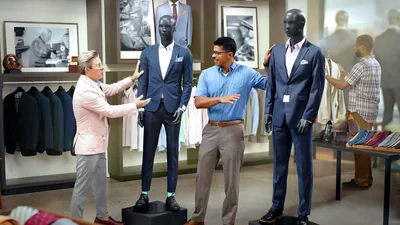 A young brother at a store, being shown a tight-fitting suit by a salesman. The brother asks about a more modest-fitting suit instead.