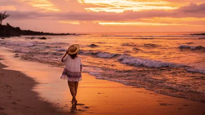 A sister watching the waves break as she walks along a beach at sunset.
