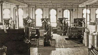 Operators standing by their linotype machines on the factory floor