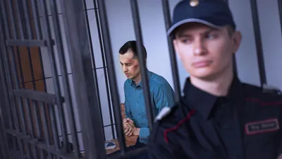 A brother with bruises on his face, praying in his prison cell as a guard stands nearby.