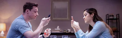 A husband and wife each using a smartphone while they are eating a meal.