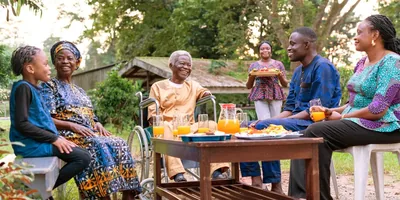 An older man who lost his arms in war, sitting in a wheelchair and enjoying a meal with his family outdoors.