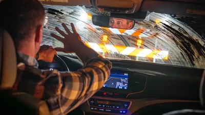 A man driving a car with a dirty windshield, surprised by a roadblock that is right in front of him.