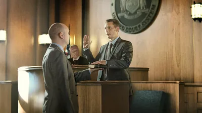 A man taking an oath in court. His right hand is raised, and his left hand is on a Bible.