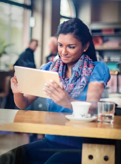 A young woman in a café reads the Bible on her electronic device