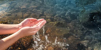 A woman lifting clear water in her hands from a stream.