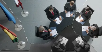 A torn photograph of a group of national leaders sitting around a table together. They all sign a copy of the same document.
