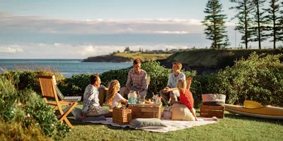 A family enjoying a picnic by the water. They are laughing and relaxing in one another’s company.