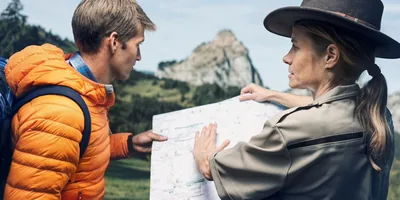 The young man pictured in the previous image getting help from a park ranger. She uses a map to show him which route to take to get to his destination, the top of a mountain.