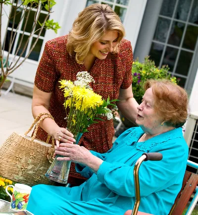 A sister giving flowers to an elderly and infirm sister.