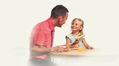 A father with his young daughter eating a meal together.