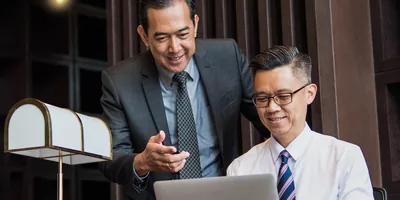 A businessman dictating a letter to a secretary who is typing it on a laptop.