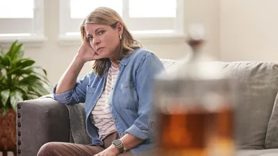 A sister sitting on her sofa, staring across the room at a bottle of alcohol.