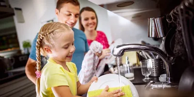 A little girl washes dishes with the help of her parents
