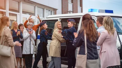 A sister being escorted into a van by two female police officers while a group of her brothers and sisters applaud her.