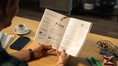A man reading lesson 40 of the “Enjoy Life Forever!” book. On his desk is a pack of cigarettes and an ashtray filled with cigarette butts.